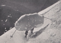 Smučar v nizkim preži z razprostrtim netopirskim plaščem na težkem snegu – boljše ravnotežje kot brez plašča (1938).