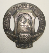 Kovinski znak zveznega učitelja smučanja, ki ga je moral učitelj smučanja obvezno na vidnem mestu, ko je učil smučanje. Na znaku so grbi Srbije, Hrvaške in Slovenije, Kraljevina Srbov Hrvatov in Slovencev ter slaba ponazoritev gore Jalovca.